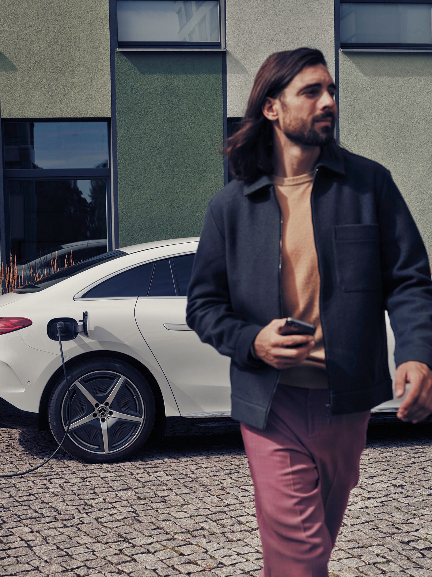 A man walking next to a charging white Mercedes-Benz EQE