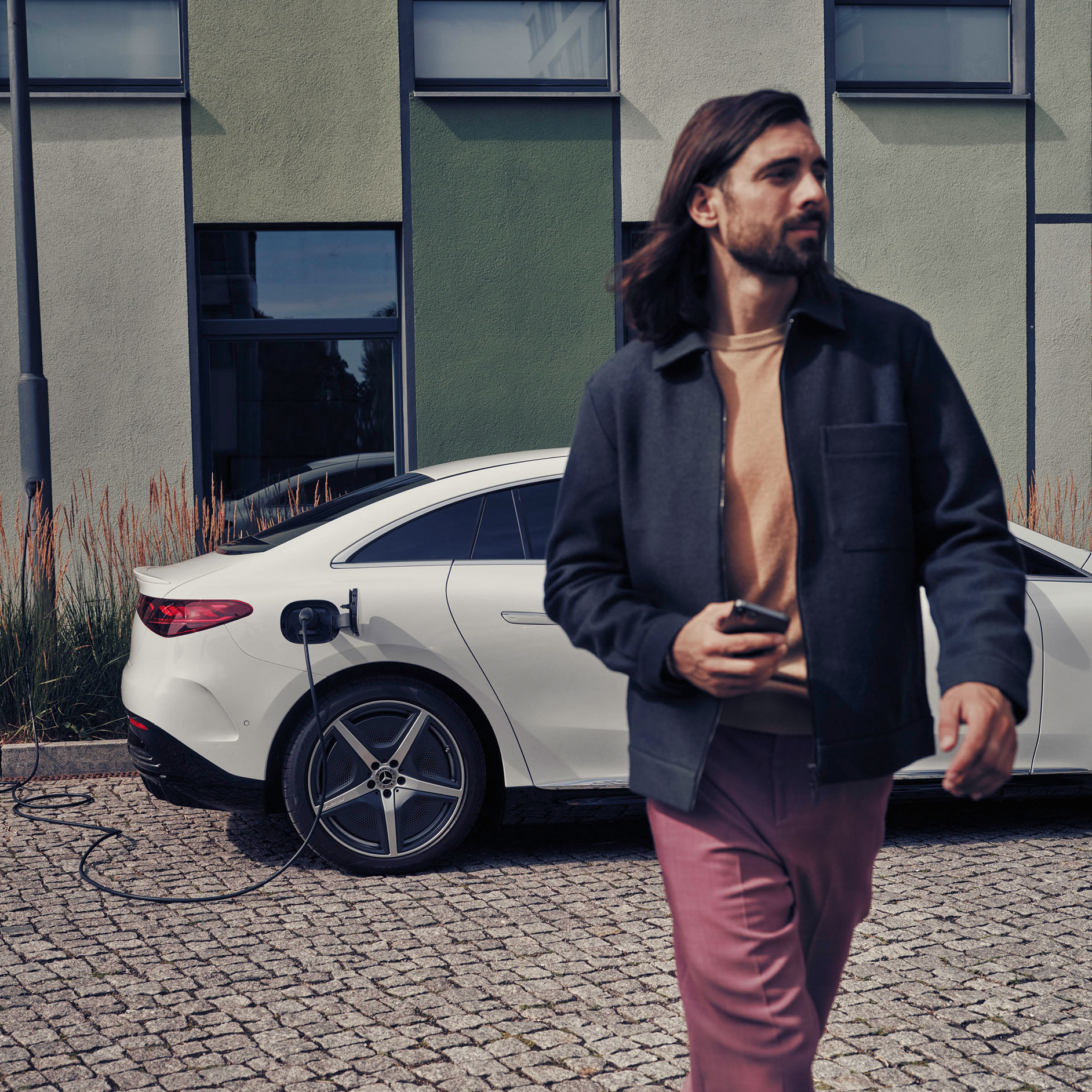 Subscription | Financial Services | Mercedes-Benz A man walking next to a charging white Mercedes-Benz EQE