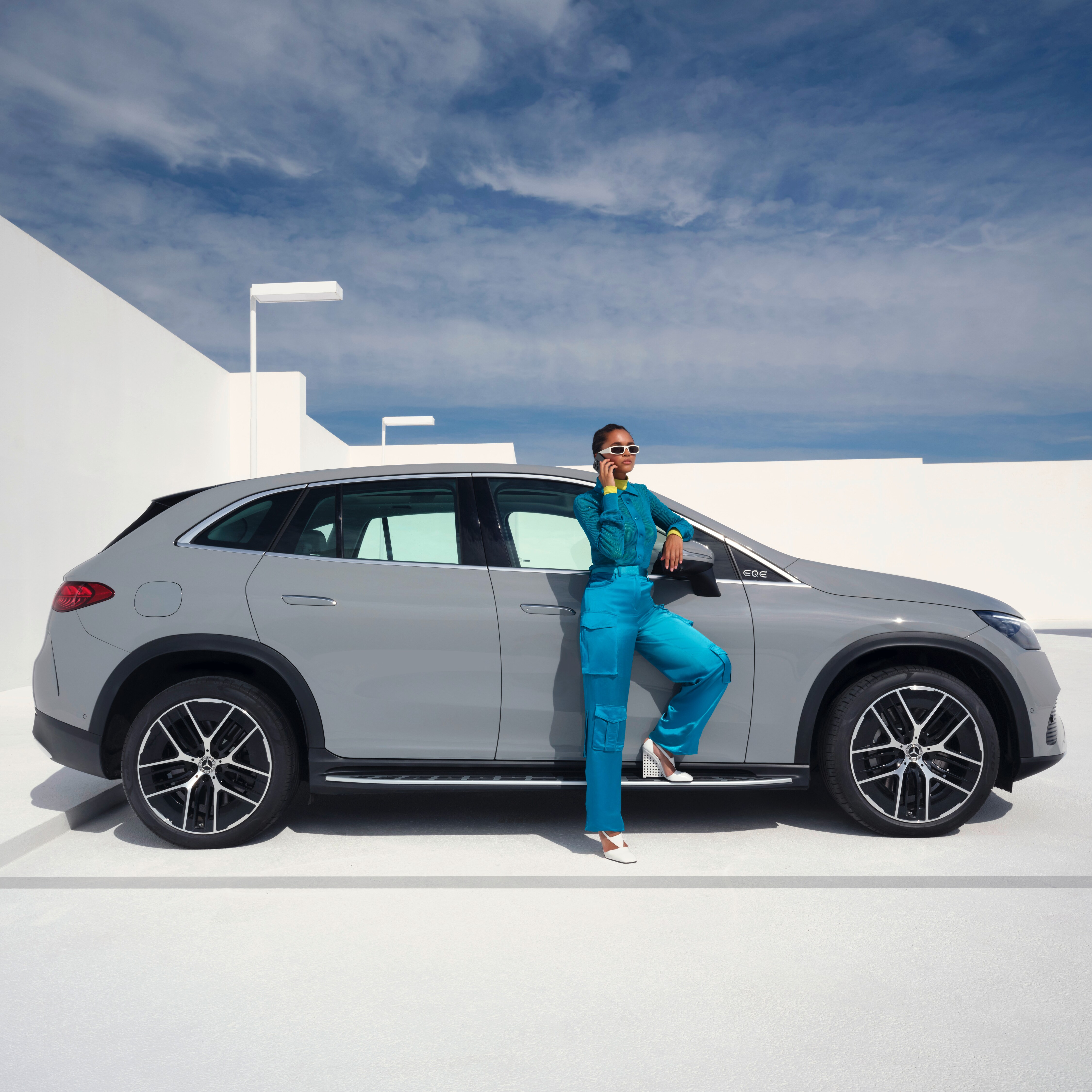 Woman standing in front of her Mercedes-Benz with her phone in her hand and being in a call