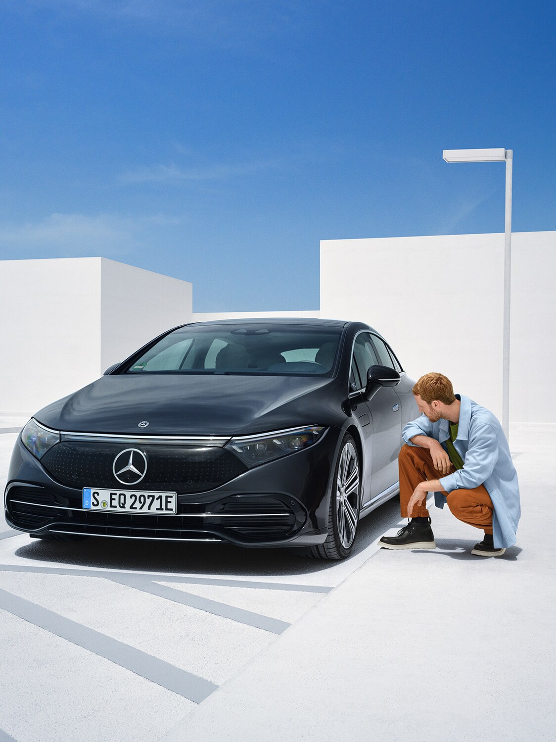 A person is kneeling on the side of his Mercedes-Benz vehicle to check on it.