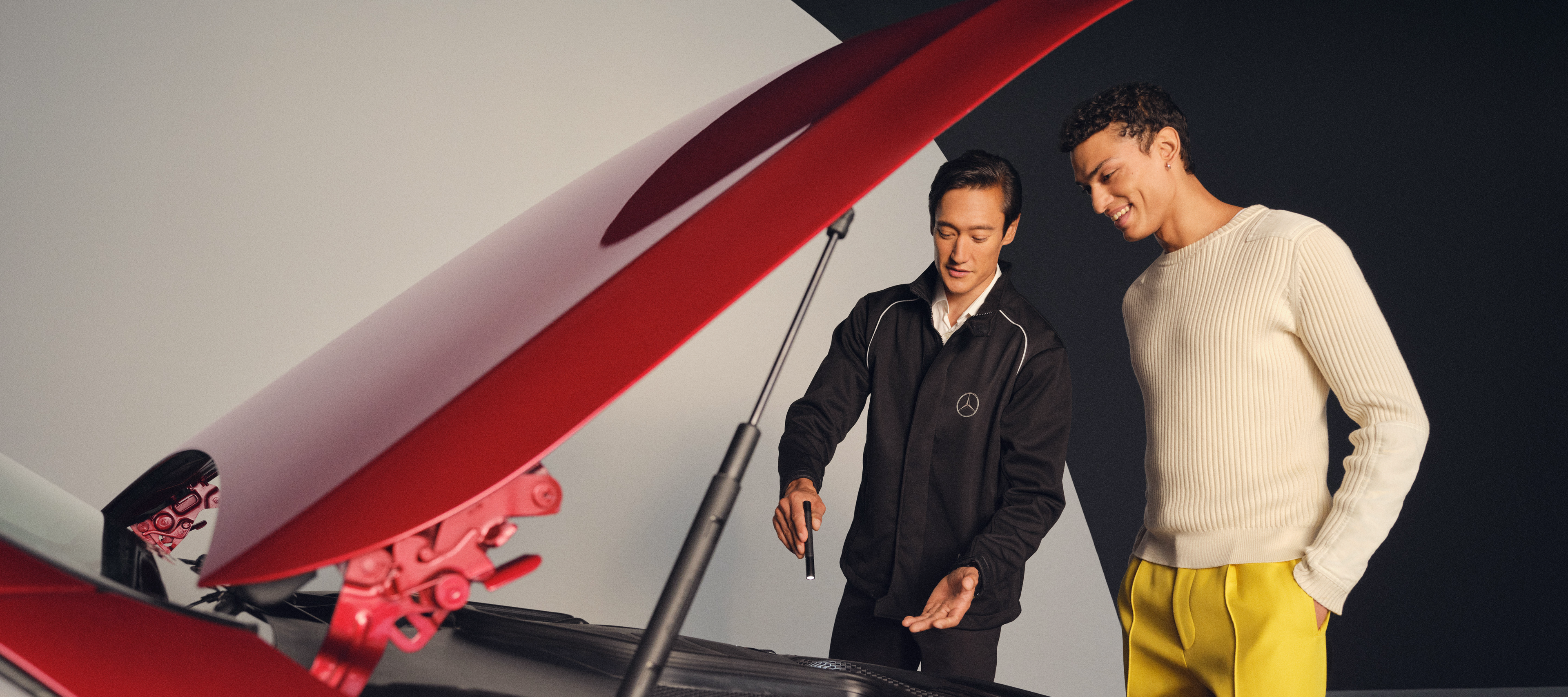 Dịch vụ bảo trì của Mercedes-Benz. Một kỹ thuật viên Mercedes-Benz và một người đàn ông đang đứng trước nắp ca-pô đang mở của một chiếc Mercedes-Benz.