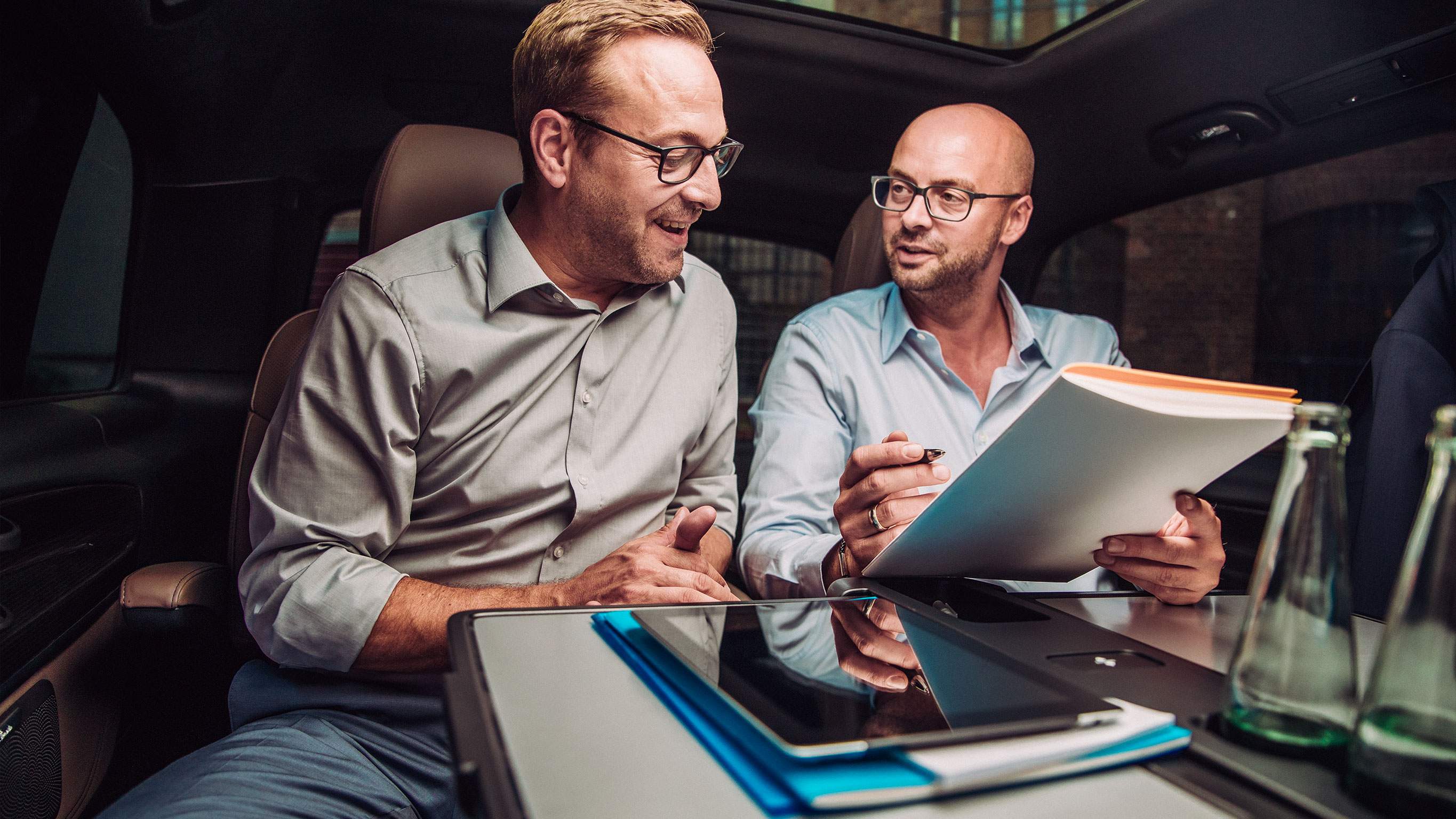 Exclusive privileges for corporates and key professional groups Two men discussing documents inside a Mercedes-Benz vehicle – Exclusive privileges for corporates and key professional groups
