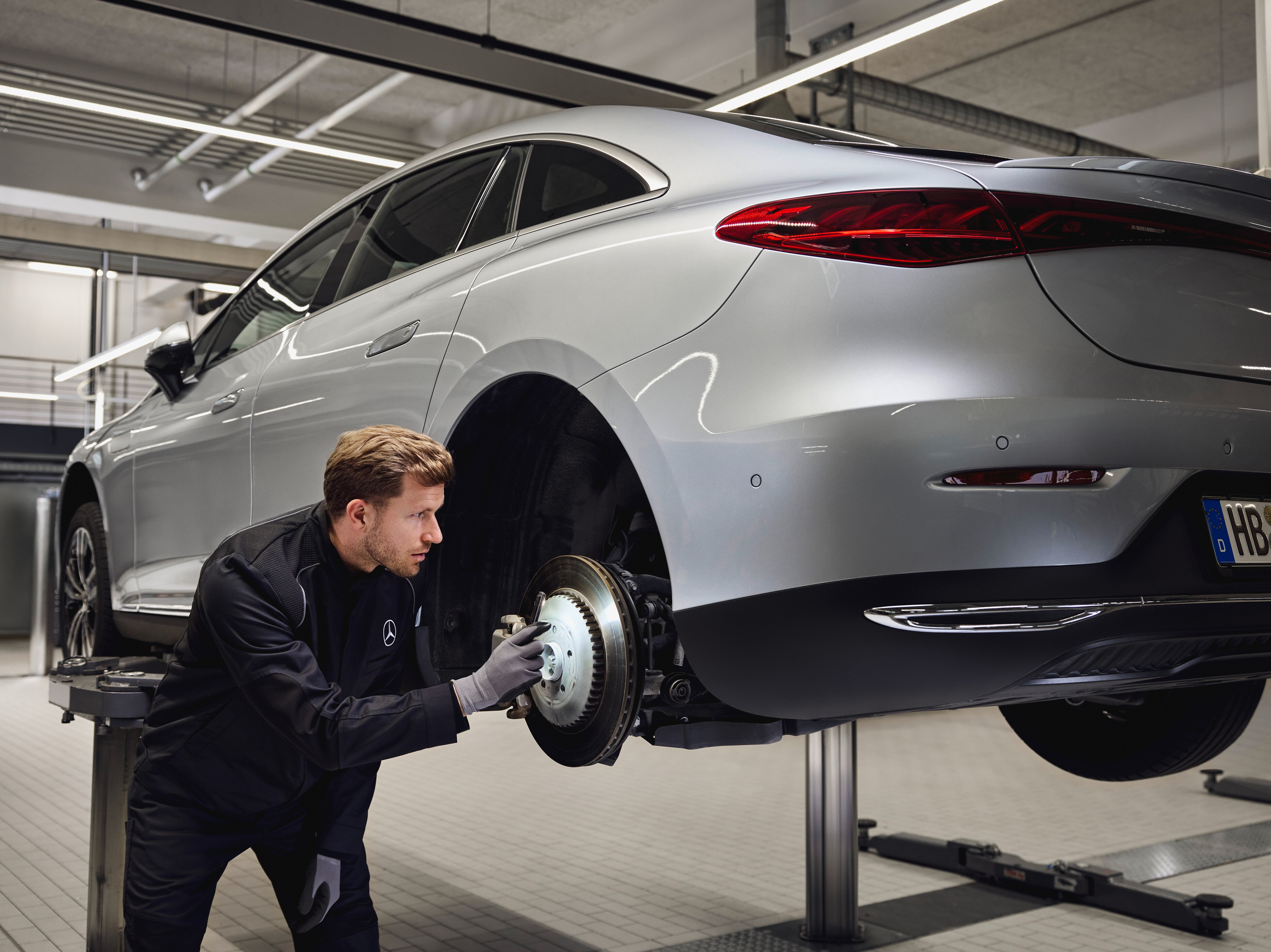 Mercedes‑Benz vehicle raised on a lift with a technician inspecting the rear brake system for a replacement of genuine parts service.