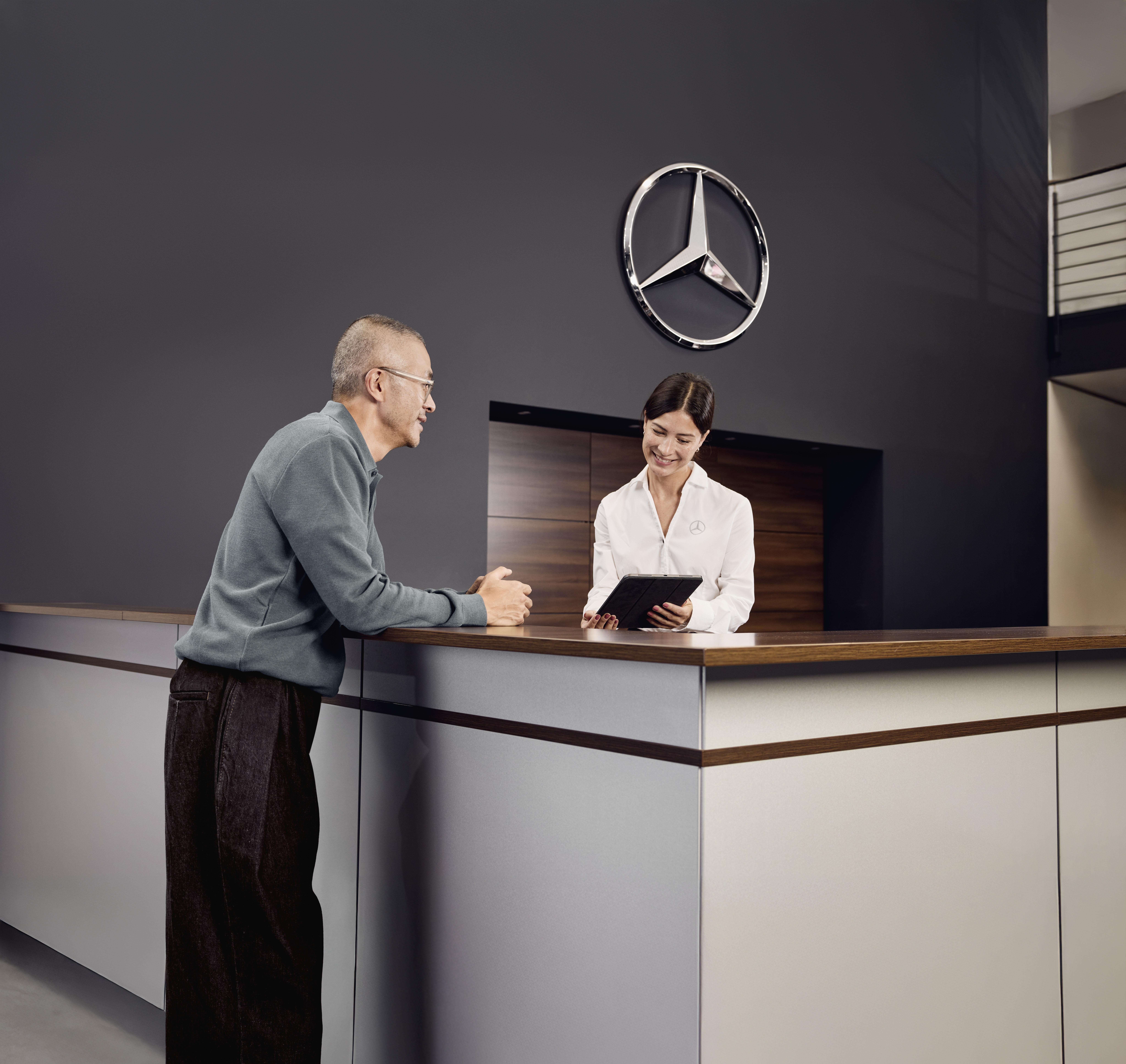 Mercedes‑Benz Genuine Parts Consultation Service reception area at a Mercedes‑Benz dealership where a customer discusses vehicle service details with a service advisor at the front desk.